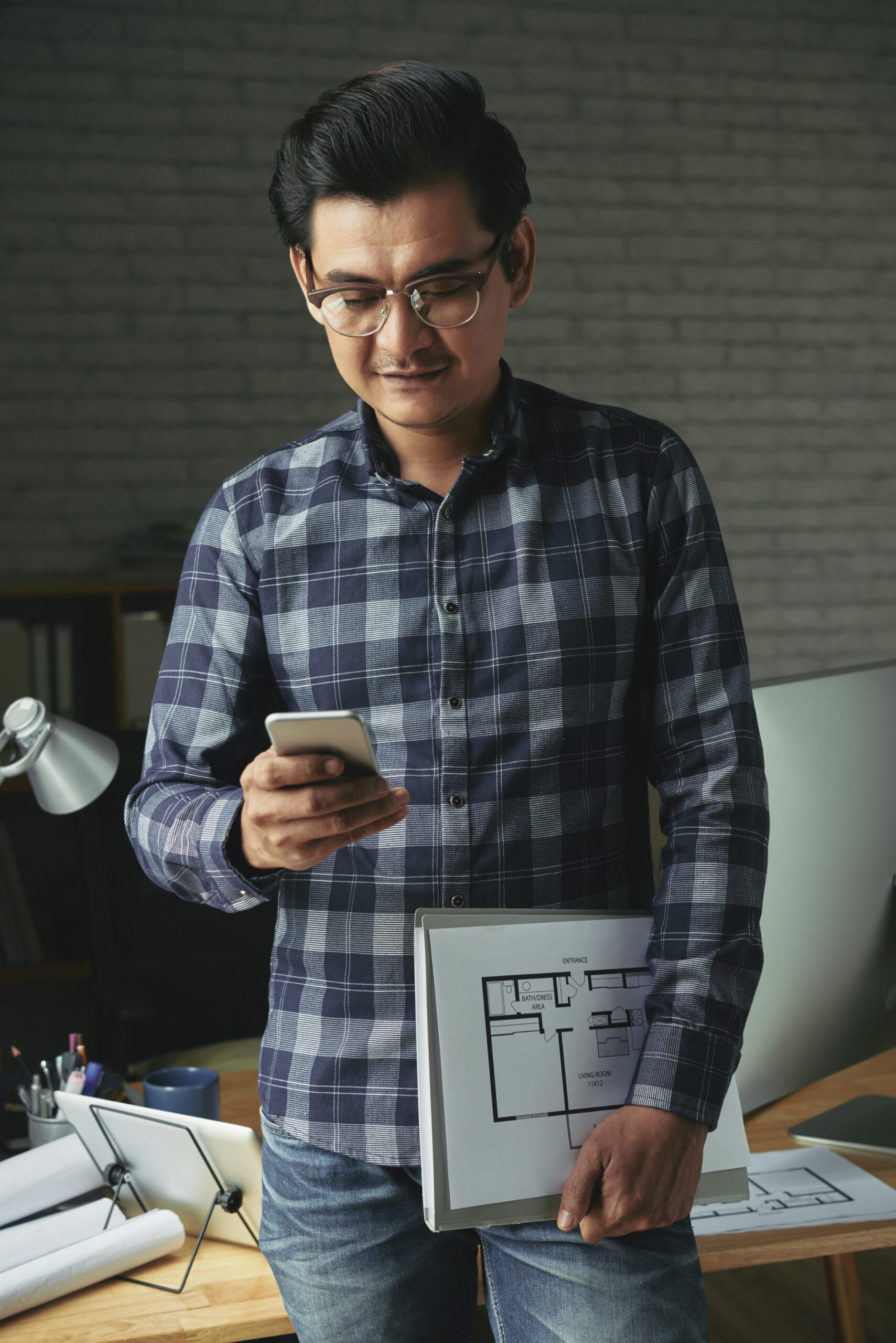 Vietnamese architect with house plan reading message on the phone